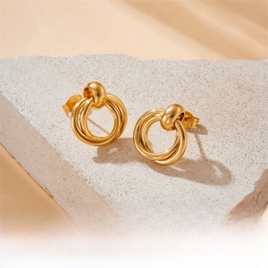 Detail of interlocking golden geometric hoop earrings on a textured stone base