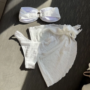 Flat lay of white smocked bikini with metal ring detail and matching sarong cover-up
