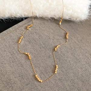 Detail of minimalist gold necklace with tiny cubic beads on a refined grey background