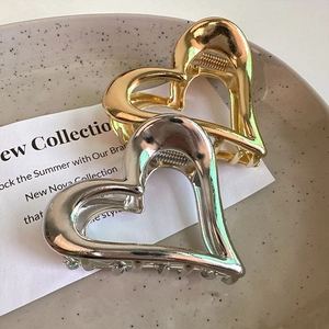 Detailed view of hollow heart metal hair claws in gold and silver on a ceramic tray