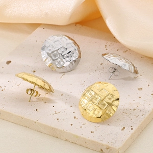 Macro detail of round textured stainless steel earrings on stone and silk background