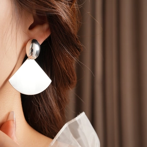 Detailed view of silver oval stud and brushed fan-shaped earrings on a model
