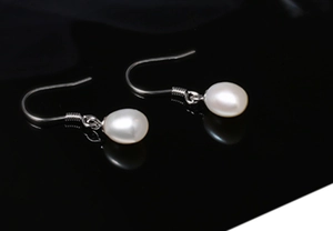Detail view of round white freshwater pearl earrings with silver ear hooks on black surface