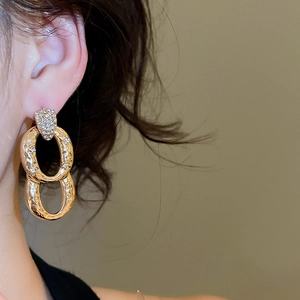 Detail of gold double oval hoop earrings with hammered metal texture and zircon accents