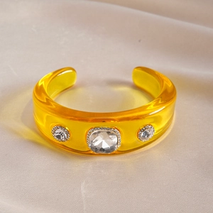 Detailed view of yellow resin cuff bracelet with square crystal on champagne silk