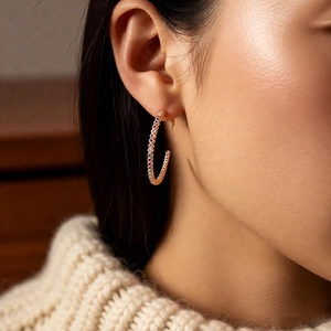 Détail de créoles en or en forme de C avec zircons colorés portées par un mannequin