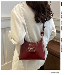 Close-up of wine red glossy shoulder bag with silver bow and decorative knot strap