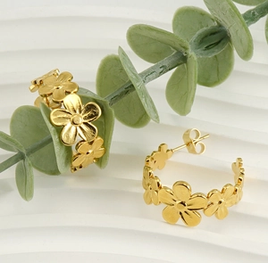 Macro detail of gold daisy floral C-shaped earrings on a white textured background