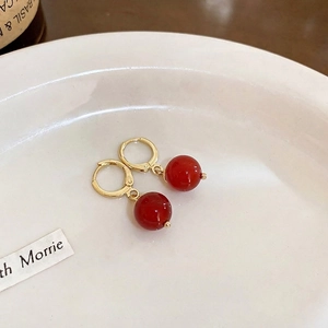 Elegante vergoldete Ohrringe mit glänzenden roten Perlen auf Keramikplatte