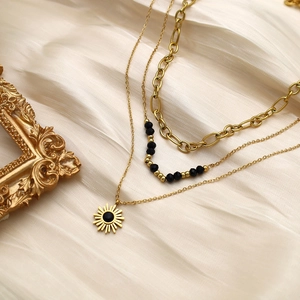 Detailed view of triple-layered golden necklace with sun pendant and black seed beads