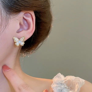 Detail of elegant gold butterfly stud earrings with pearl white enamel on model ear
