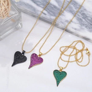 Gros plan de pendentifs cœur en zircon noir, rose et vert avec une chaîne à billes dorée