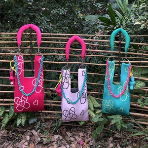 Detailed view of colorful knit tote bags with thick chain straps on a bamboo fence