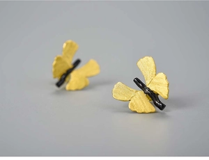 Macro detail of butterfly stud earrings featuring matte gold wings and black body texture
