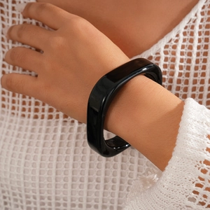 Macro shot of chunky black resin geometric bangle with polished mirror finish texture