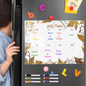 Close-up of magnetic acrylic weekly planner with autumn leaves on a dark refrigerator