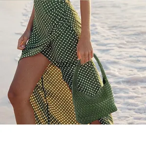 Detail of green woven leather hobo bag held by a model in a polka dot dress