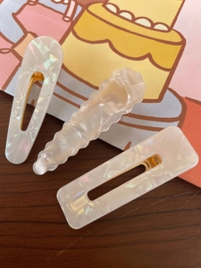 Close-up of three cream-colored geometric hair clips with gold metal base on wood