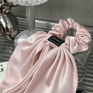 Pink satin bow scrunchie with silk luster and handmade label on a modern display