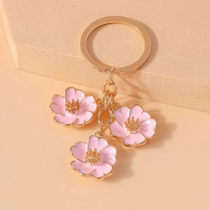Close-up of golden keychain with three pink cherry blossom pendants on a soft beige surface