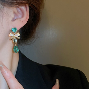 Détail de boucles d'oreilles nœud et cœur avec pierres vertes portées par un mannequin