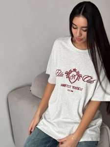T-shirt oversize gris clair avec broderie rouge porté par un mannequin sur un canapé