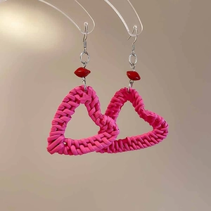 Detailed view of pink woven resin heart earrings with red bead and silver needle hook