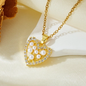 Detail of gold heart pendant with inlaid pearls and zircon on a dainty cross chain