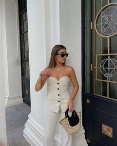 Detail of cream strapless vest with black buttons and matching high-waisted trousers