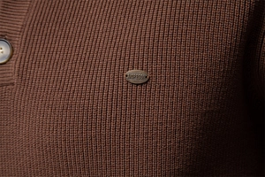 Detailed view of dark brown knit fabric with premium metal logo plate and resin button