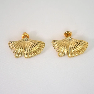 Detail view of gold ginkgo leaf earrings with frosted metal texture on white fabric