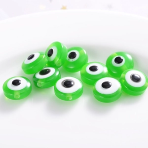 Detailed view of green flat round evil eye resin beads scattered on a white ceramic dish