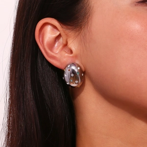 Macro shot of silver oval earrings with colorful zircon stones on female ear