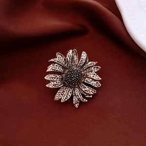 Detail of vintage sunflower brooch with textured bronze petals on dark velvet background