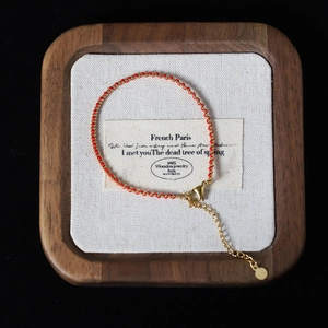 Detailed view of red braided rope bracelet with gold beads on a wooden jewelry tray