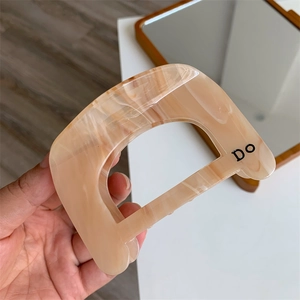 Detail of light orange acetate hair claw clip with marble texture and letter D design