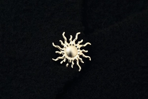 Macro shot of sun-shaped golden metal button on a black textured knit fabric background