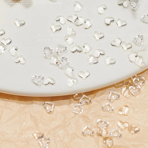 Transparent heart nail art charms with solid and hollow designs on a ceramic plate