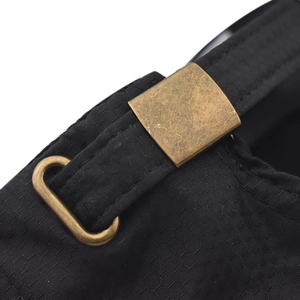 Detail of the adjustable bronze metal buckle and textured black fabric on the hiking cap