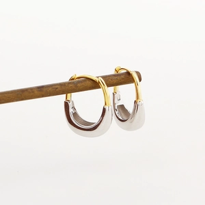 Dettaglio degli orecchini a forma di U bicolore oro e argento su supporto di legno