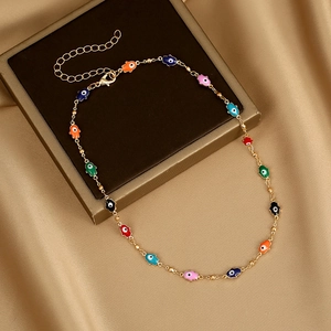 Detail of gold necklace with colorful enamel Evil Eye and Hamsa Hand charms on satin