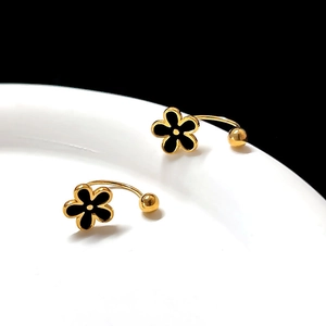 Macro detail of gold flower stud earrings with black enamel petals on white ceramic