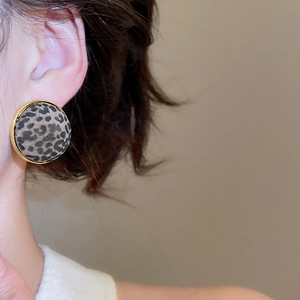 Close-up of leopard print round earrings with gold trim worn by a model in soft light