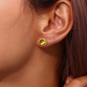 Close-up of a model wearing a gold sunburst earring with a green cat-eye stone