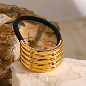Minimalist gold metal cylinder hair tie with black elastic band on natural stone base