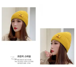 Detail view of yellow chunky knit beanie with decorative text patch on thick brim