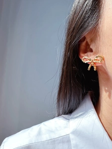 Close-up of a model wearing a golden bow stud earring with a unique cubic woven texture