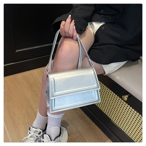 Close-up of a silver minimalist leather handbag held by a model in a modern interior