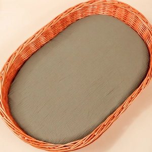 Detail of olive cotton gauze crib sheet with natural crinkle texture on woven bassinet
