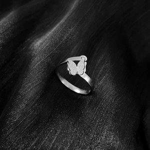 Minimalist silver butterfly titanium steel ring on dark textured fabric background